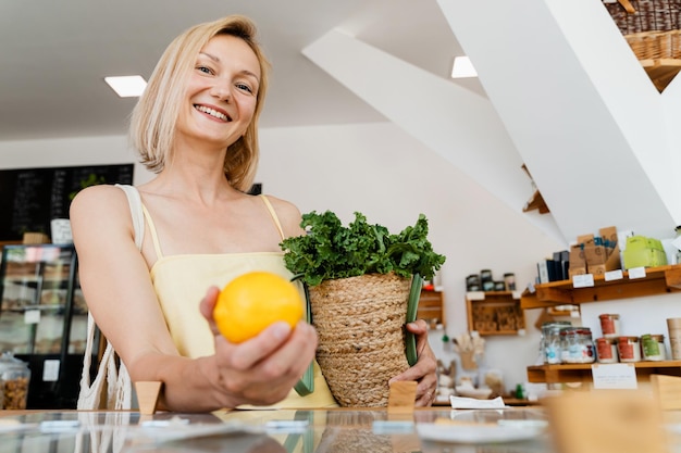 Donna sorridente che compra cibo biologico e prodotti ecologici in un negozio sostenibile privo di plastica