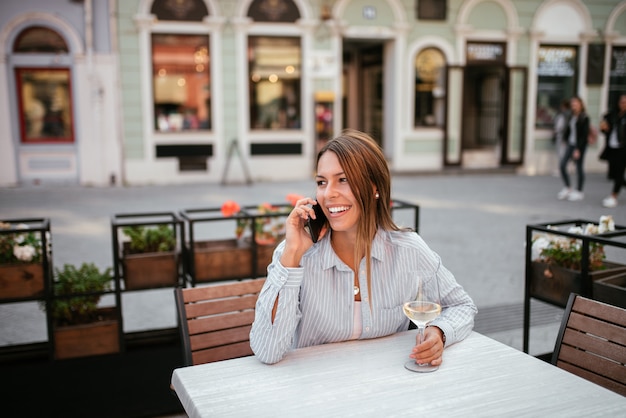 Donna sorridente che comunica sul telefono nel caffè all&#39;aperto.