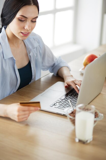 Donna sorridente che fa shopping online utilizzando il computer e la carta di credito in cucina