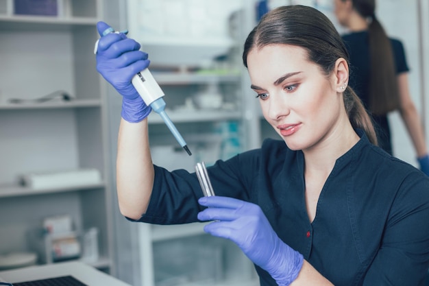 Donna sorridente che guarda la provetta in mano mentre usa un erogatore di pipette automatiche