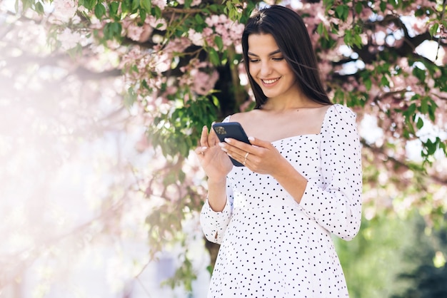 Donna sorridente che indossa un abito bianco utilizzando smartphone ragazza utilizzando l'applicazione di social media