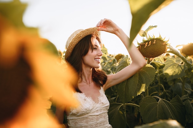 Donna sorridente che indossa un cappello in piedi in un campo di girasoli al tramonto