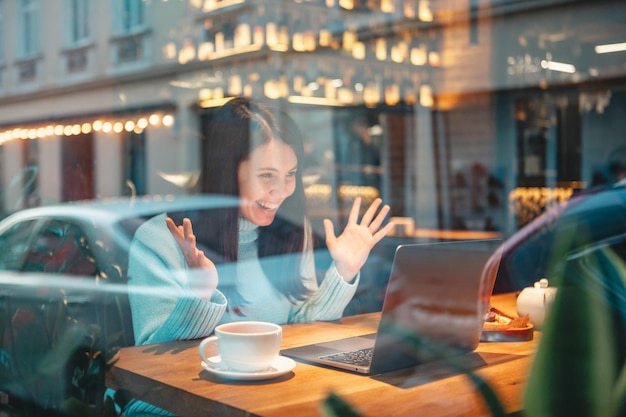 Donna sorridente che lavora al computer portatile nel ristorante che beve il tè che mangia la vista dell'hamburger attraverso il vetro