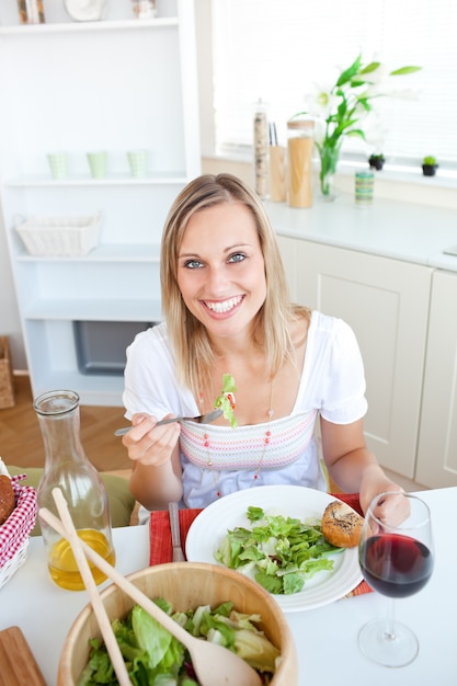 Donna sorridente che mangia insalata nella cucina