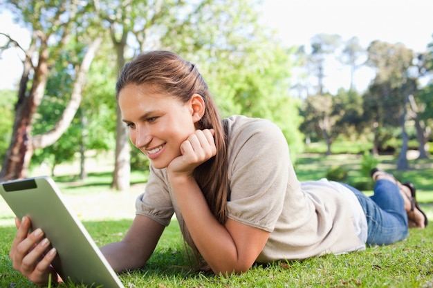 Donna sorridente che pone sul prato inglese con il suo computer tablet