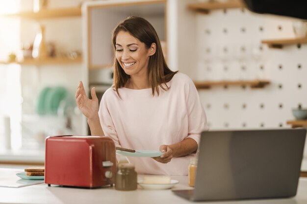 Donna sorridente che prepara la colazione per se stessa, tostando il pane a casa.