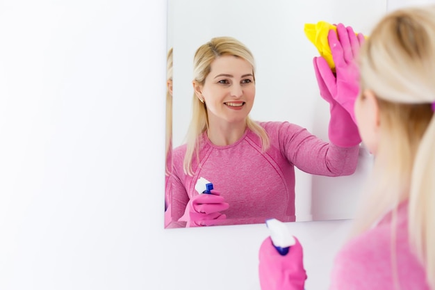 Donna sorridente che pulisce uno specchio in un bagno a casa