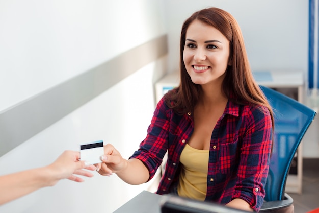 Donna sorridente che si siede nell'ufficio che prende carta di credito e sguardo felice