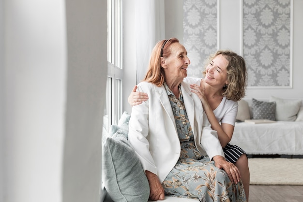 Donna sorridente che si siede sul davanzale della finestra con la nonna a casa