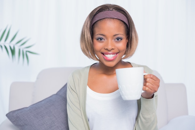 Donna sorridente che si siede sul sofà che tiene tazza di caffè