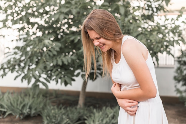 Donna sorridente che sta nel parco che ha dolore di stomaco