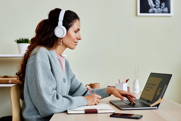 Donna sorridente che studia online a casa indossando le cuffie