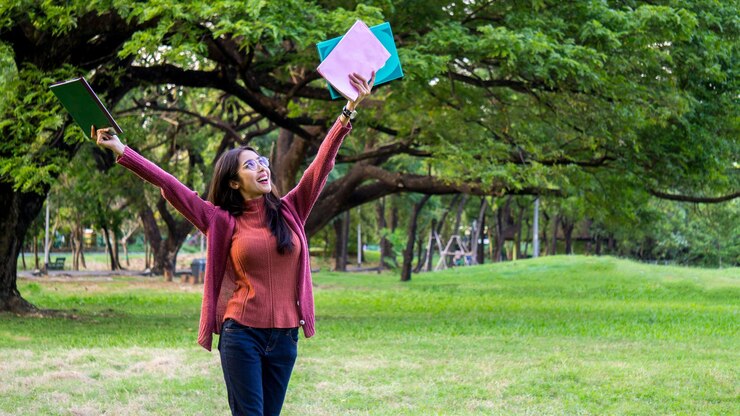 Foto donna sorridente che tiene i libri mentre cammina sul campo erboso al parco