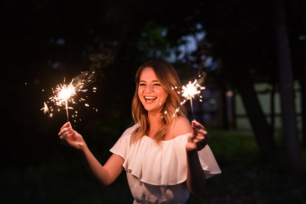 Donna sorridente che tiene sparkler e festeggia all'aperto