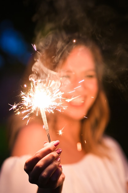 Donna sorridente che tiene sparkler e festeggia all'aperto