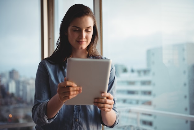 Donna sorridente che tiene tavoletta digitale mentre fa una pausa dalla finestra