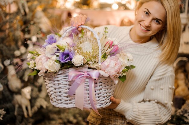 Donna sorridente che tiene un cesto di vimini di teneri fiori bianchi, rosa e viola