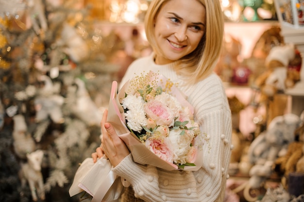 Donna sorridente che tiene un mazzo di rose rosa peonia tenera decorato con piccoli rami e foglie verdi