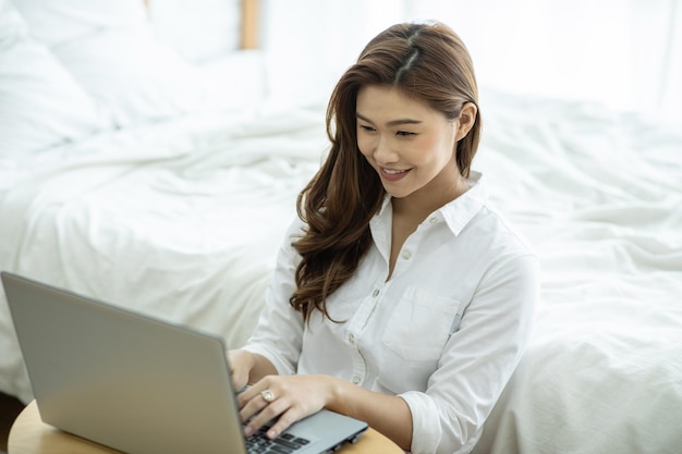 Donna sorridente che usa il portatile mentre è seduta accanto al letto a casa
