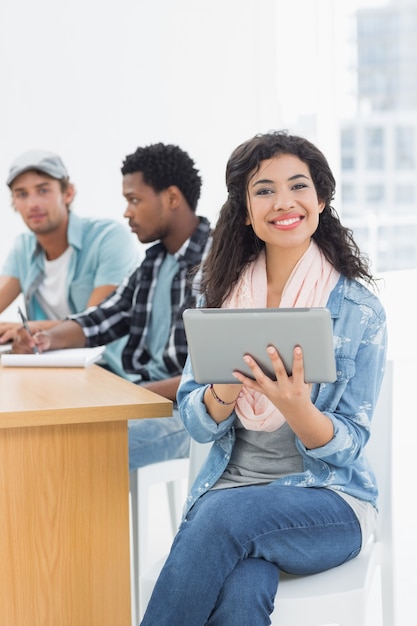 Donna sorridente che utilizza compressa digitale con i colleghi dietro nell&#39;ufficio