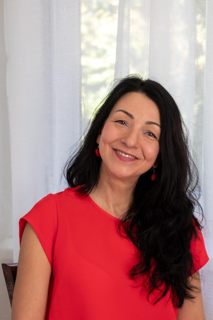 Foto donna sorridente con abito rosso capelli lunghi e scuri seduta accanto a tende luminose concetto di umore luminoso e caldo
