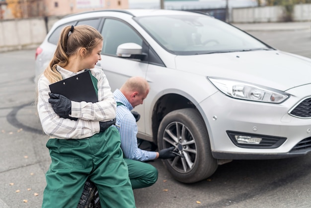 Donna sorridente con appunti e lavoratore cambiando la ruota di un'auto