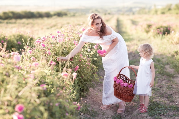 Donna sorridente con bambina che raccoglie rose nel cestino all'aperto