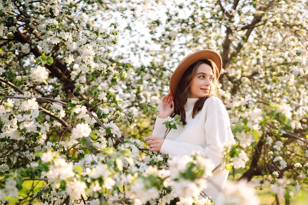 Donna sorridente con cappello in posa nel parco di primavera in fiore Il concetto di viaggio relax Stile di moda