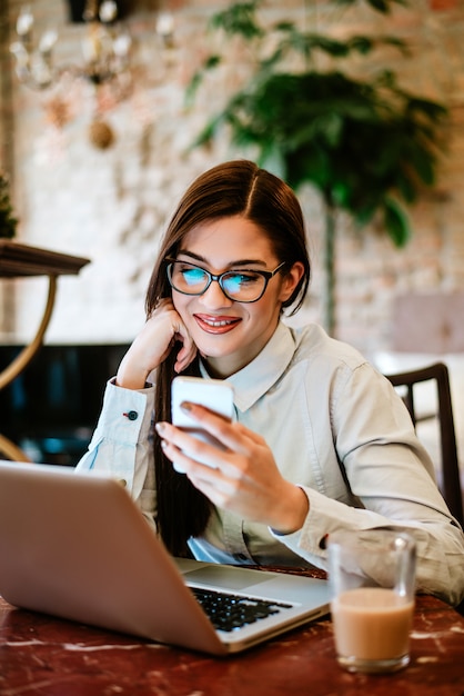 Donna sorridente con gli occhiali utilizzando smartphone e laptop.