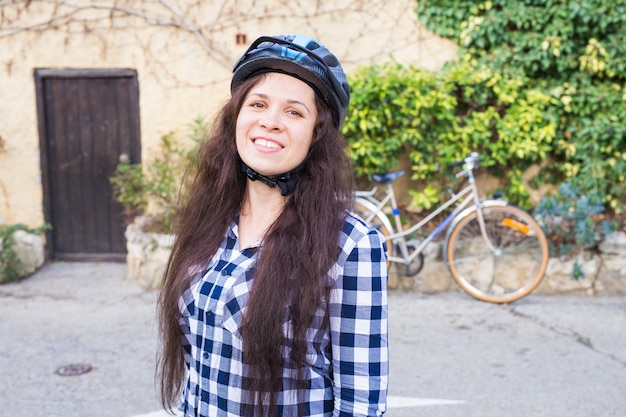 Donna sorridente con il casco contro la bicicletta e il vicolo