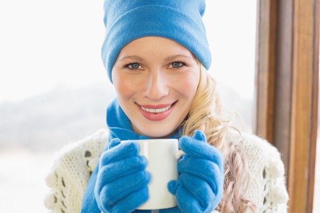 Donna sorridente con la tazza in vestiti caldi contro la finestra