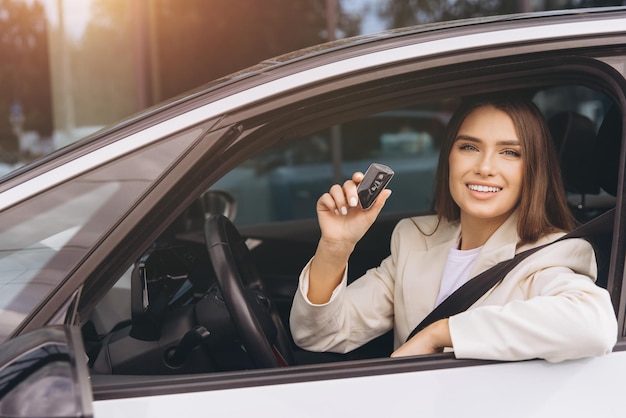 Donna sorridente con le chiavi dell'auto all'interno di un veicolo nuovo
