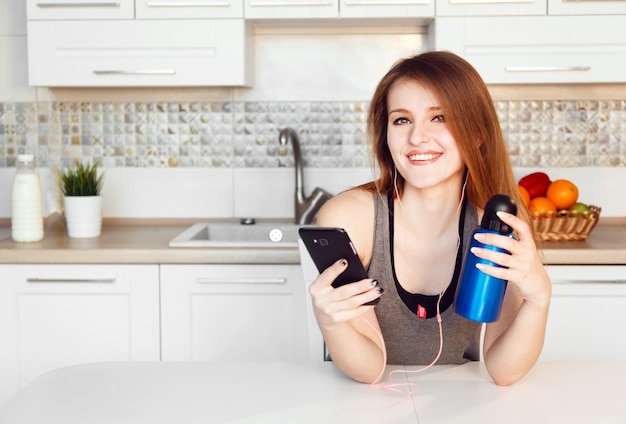 Donna sorridente con smartphone e bottiglia d'acqua in cucina