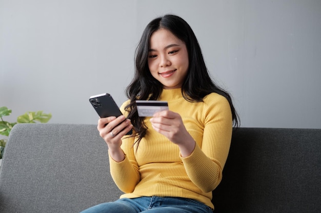 Donna sorridente con smartphone e carta di credito bancaria coinvolta nello shopping mobile online a casa, donna felice che acquista beni o servizi su Internet