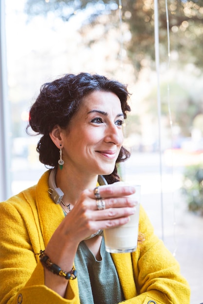 Donna sorridente con un bicchiere da cappuccino in mano che distoglie lo sguardo