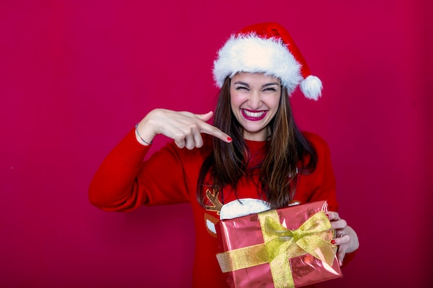 donna sorridente con un cappello da Babbo Natale e un maglione con le renne di Natale che punta a un regalo in mano