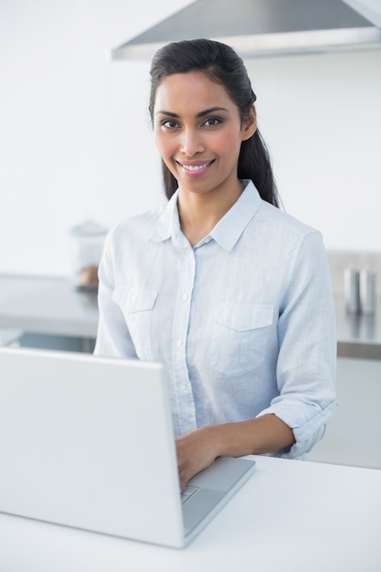 Donna sorridente contenta che scrive sul suo computer portatile che sorride alla macchina fotografica