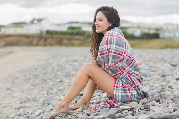 Donna sorridente coperta con coperta in spiaggia