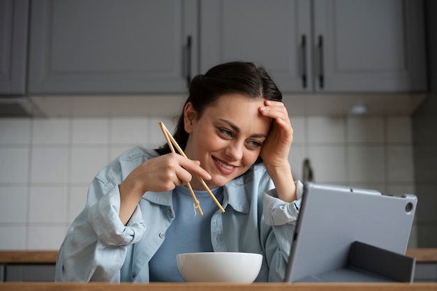 Donna sorridente del colpo medio che mangia con la compressa