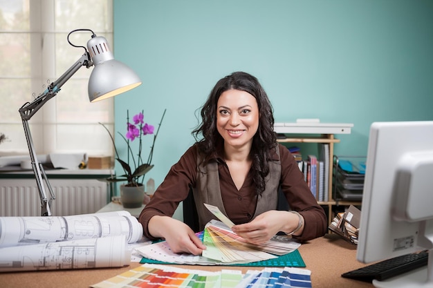 Donna sorridente dell'architetto nel suo ufficio con le carte di colore davanti a lei. Architettura e costruzione. Tavolozza dei colori