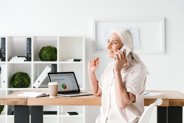 Donna sorridente di affari maturi che parla sul telefono cellulare