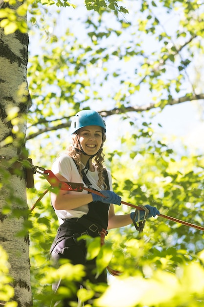 Donna sorridente di avventura della corda che sta sul supporto in alto intorno agli alberi