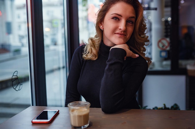 Donna sorridente di buon umore con una tazza di caffè seduto in un caffè scuro interni serali incontri in un caffè