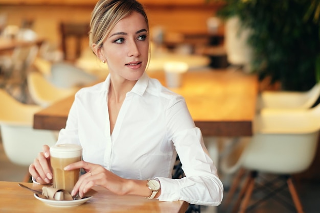 Donna sorridente di buon umore con una tazza di caffè seduto nella caffetteria