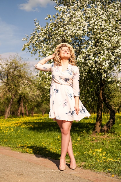 Donna sorridente di estate con il cappello di paglia nel parco - giardino delle mele nella giornata di sole primaverile