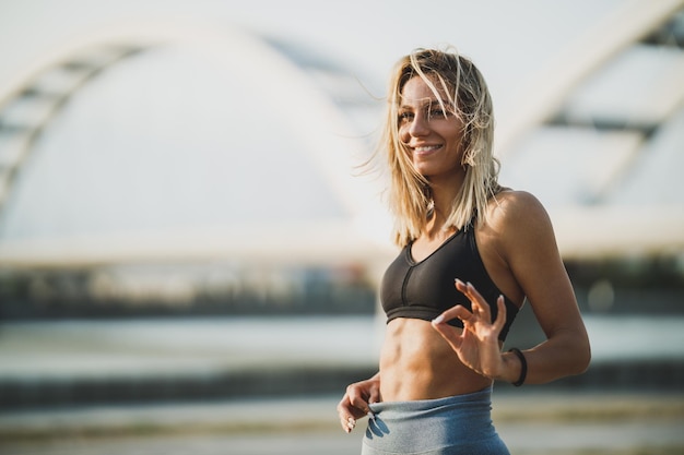 Donna sorridente di forma fisica che mostra i suoi muscoli addominali perfetti mentre si allena vicino al fiume.