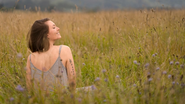 Donna sorridente di vista posteriore che si siede sull'erba