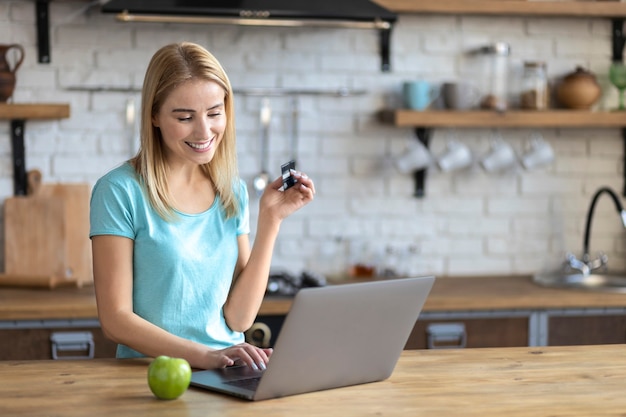 Donna sorridente felice che fa shopping online a casa in cucina