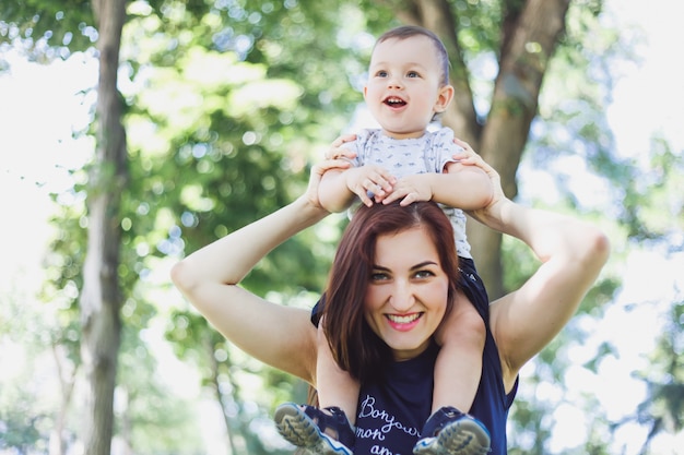 Donna sorridente felice che tiene il suo bambino sulle sue spalle nel parco