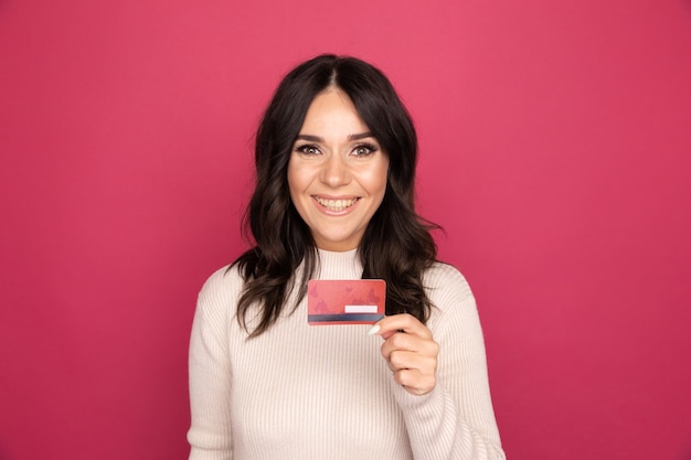 Donna sorridente felice che tiene la carta di credito isolata sullo sfondo rosa.